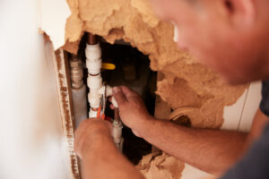 Over,shoulder,view,of,middle,aged,man,repairing,burst,pipe